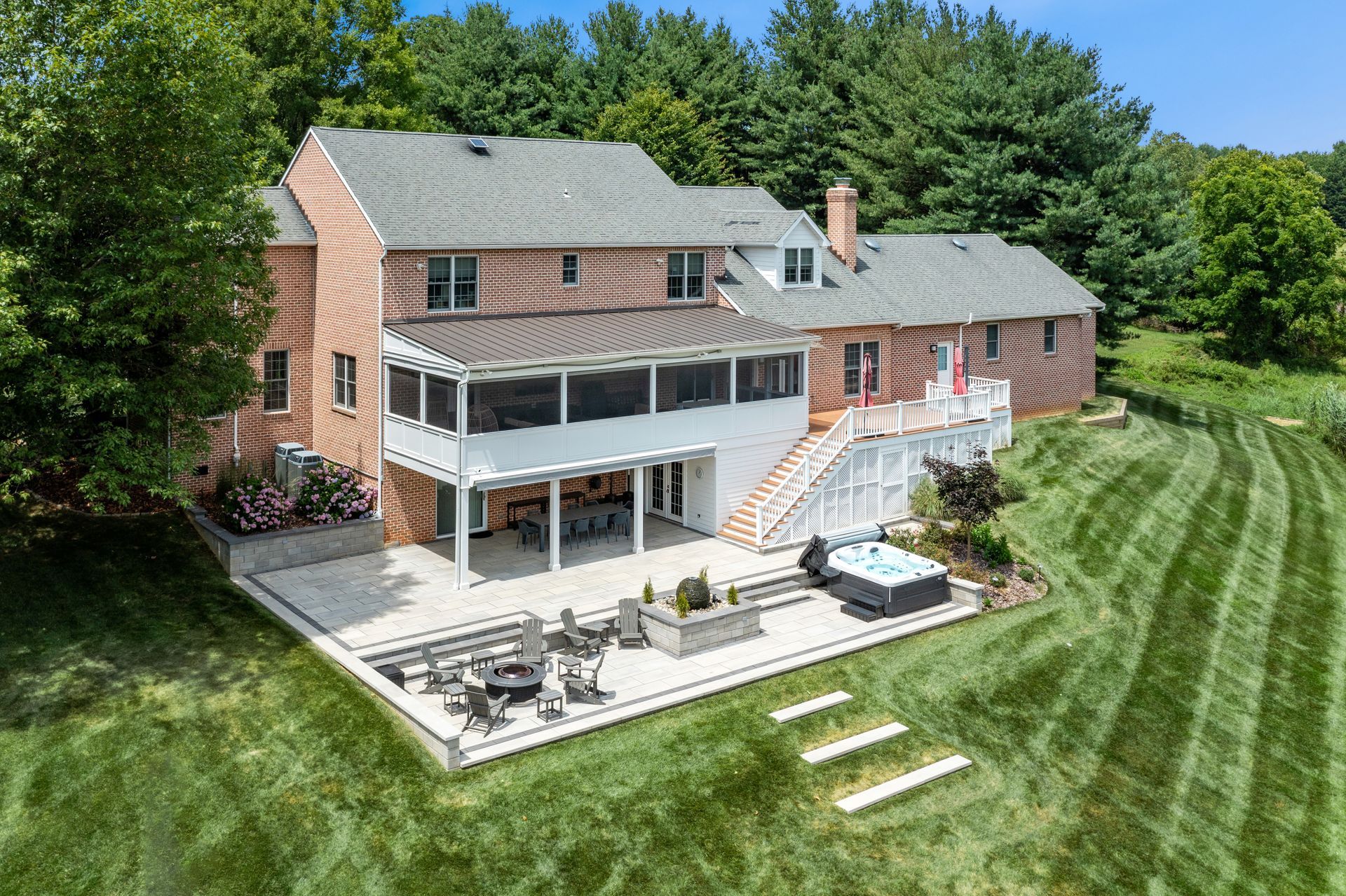 Aerial view of a brick house with a large deck and screened porch beside a mowed lawn and trees
