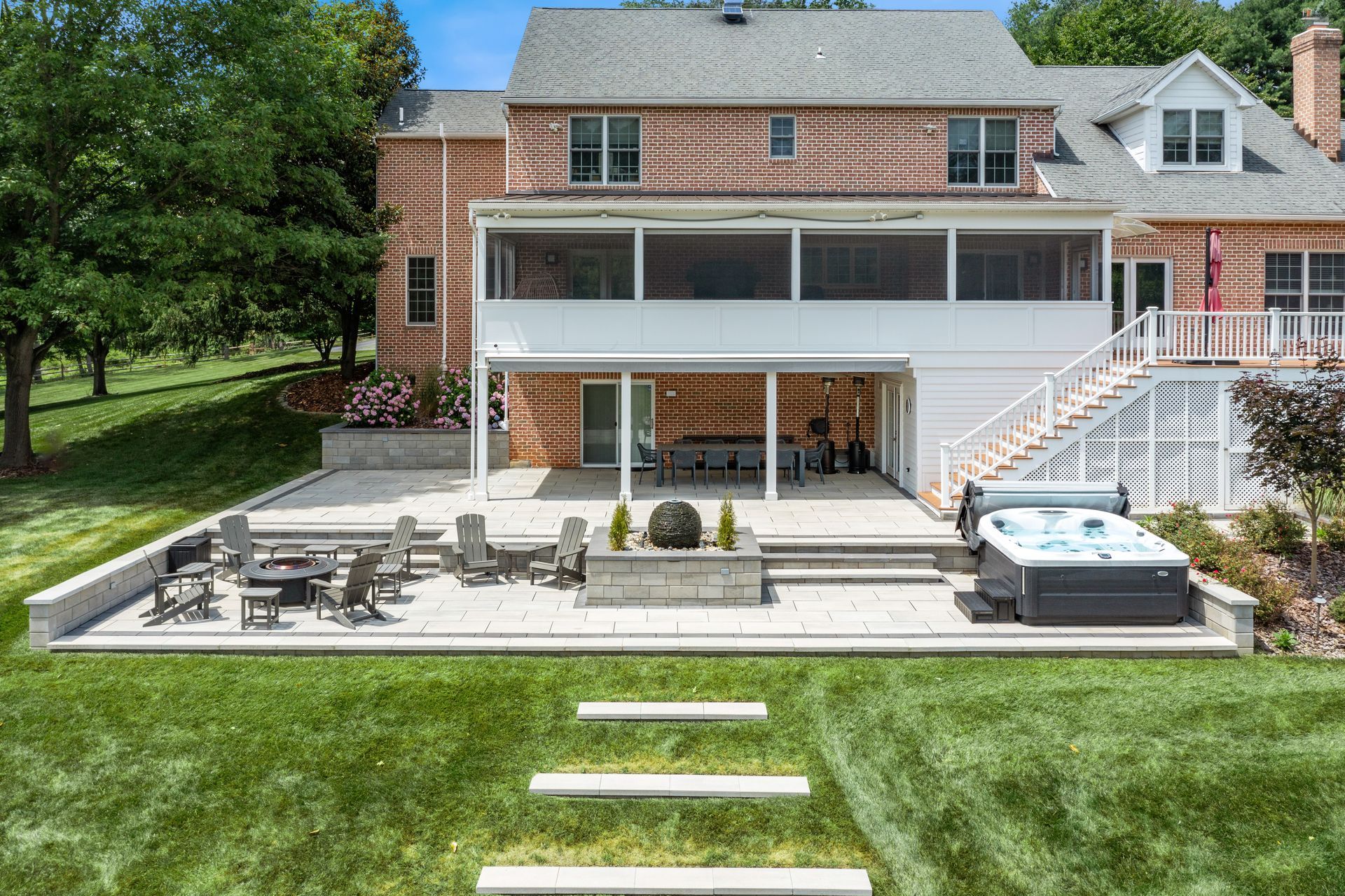 Backyard patio with outdoor dining table, lounge chairs, and a hot tub beside a brick house