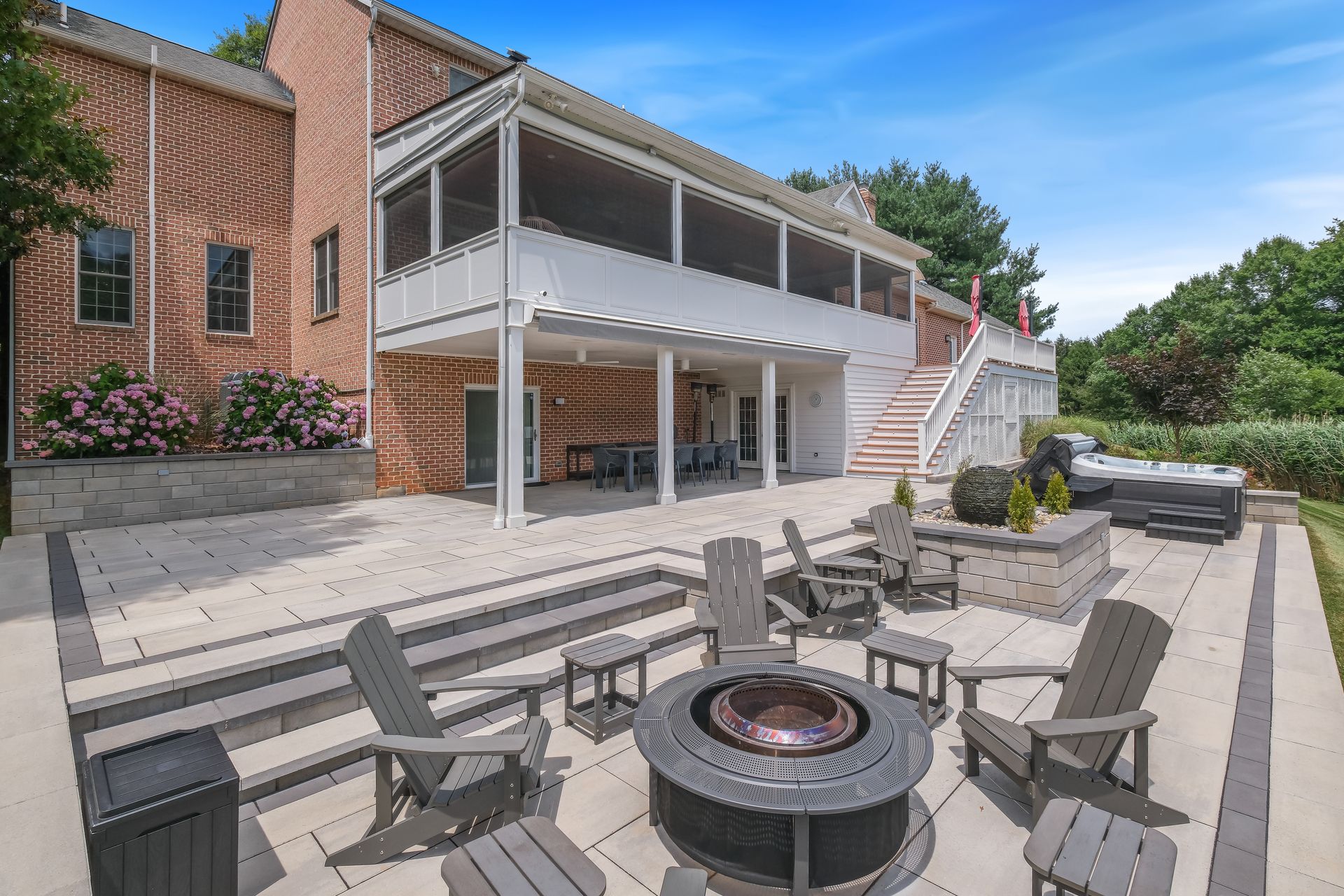 Patio with fire pit and chairs beside a brick house with raised deck and stairs