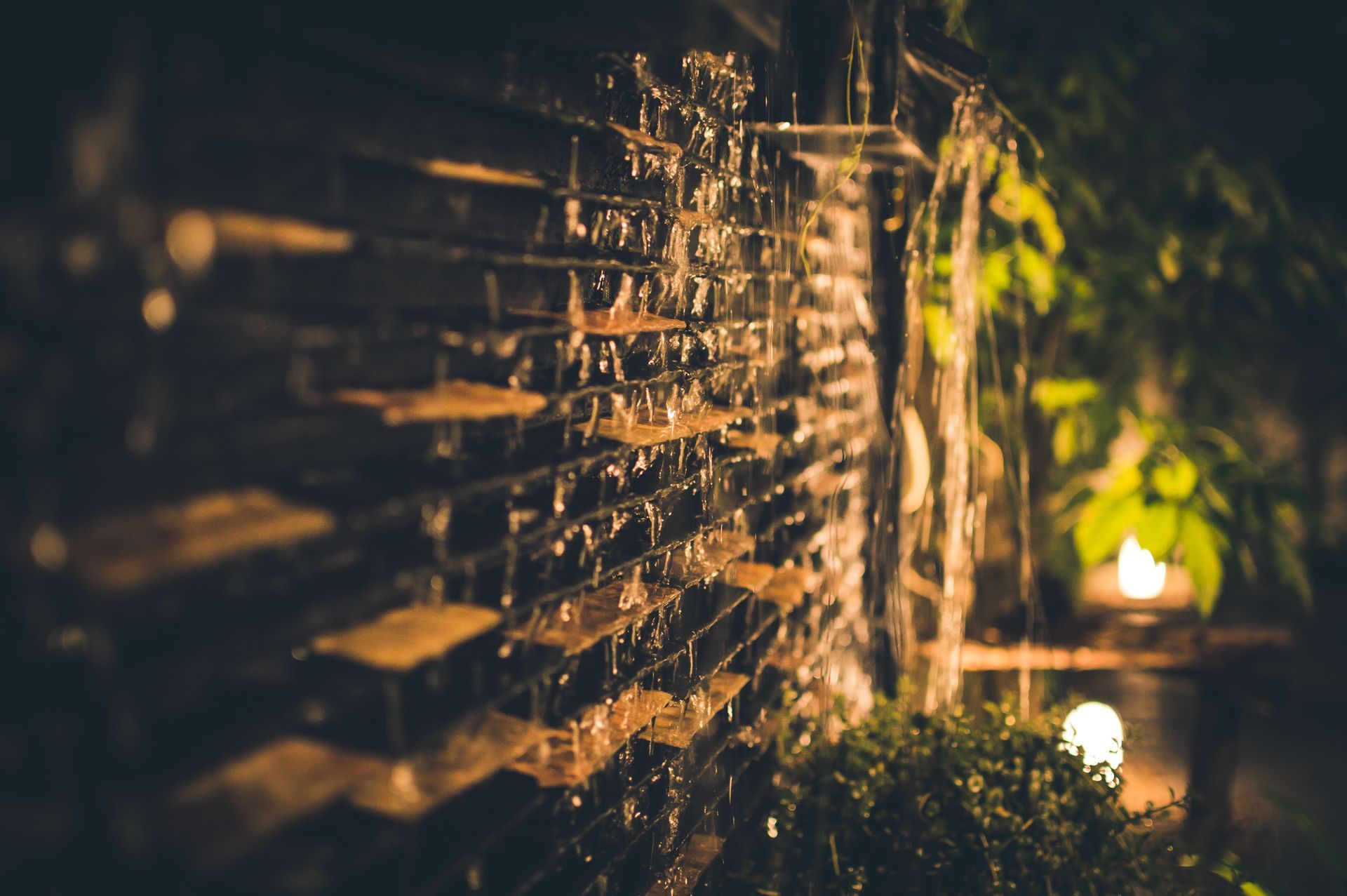 Sunlit water streaming down a wooden fence in a dim garden with warm bokeh lights