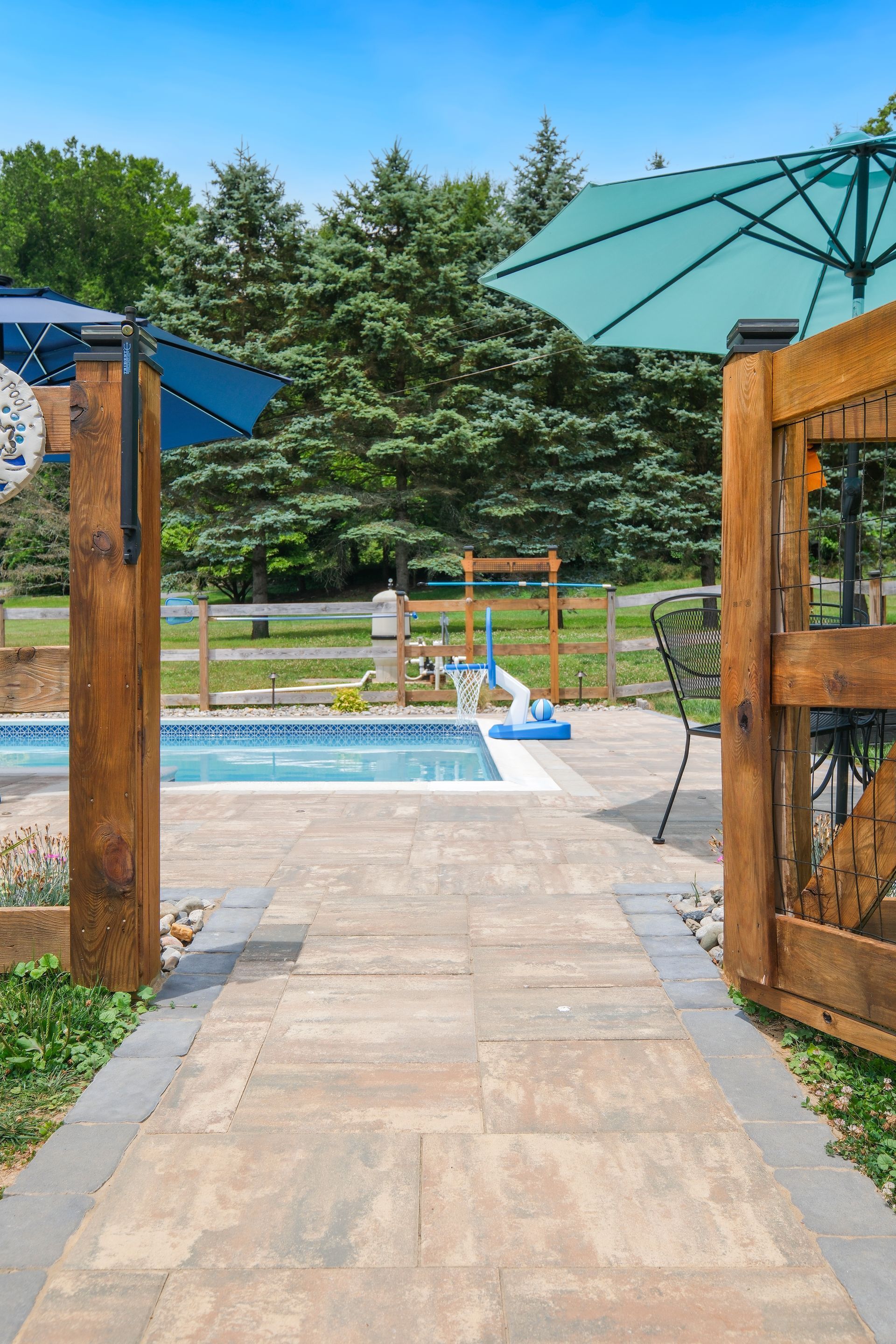 Wooden gate opening to a pool deck with green umbrella and trees beyond