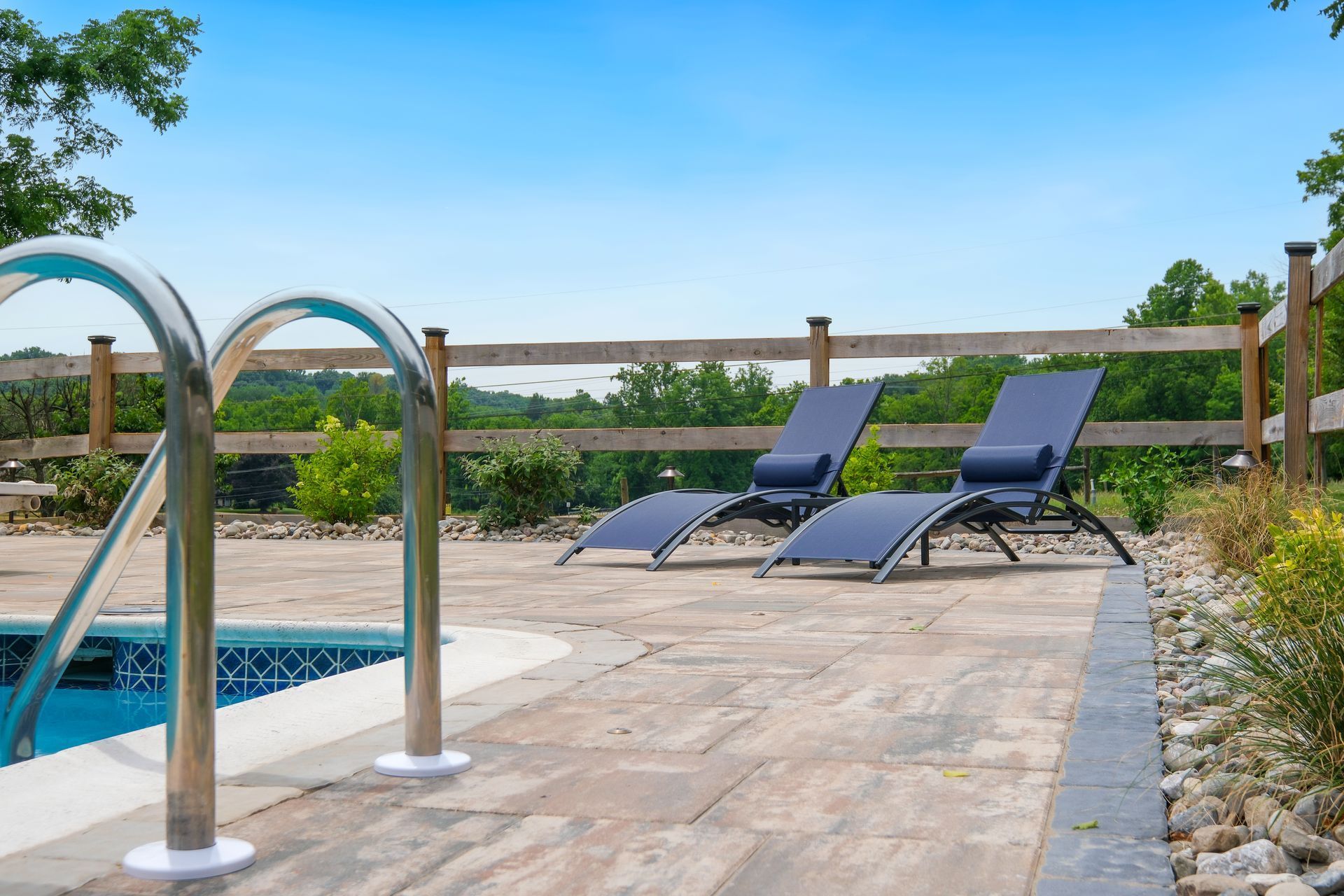 Poolside patio with two blue lounge chairs and metal handrails beside a swimming pool