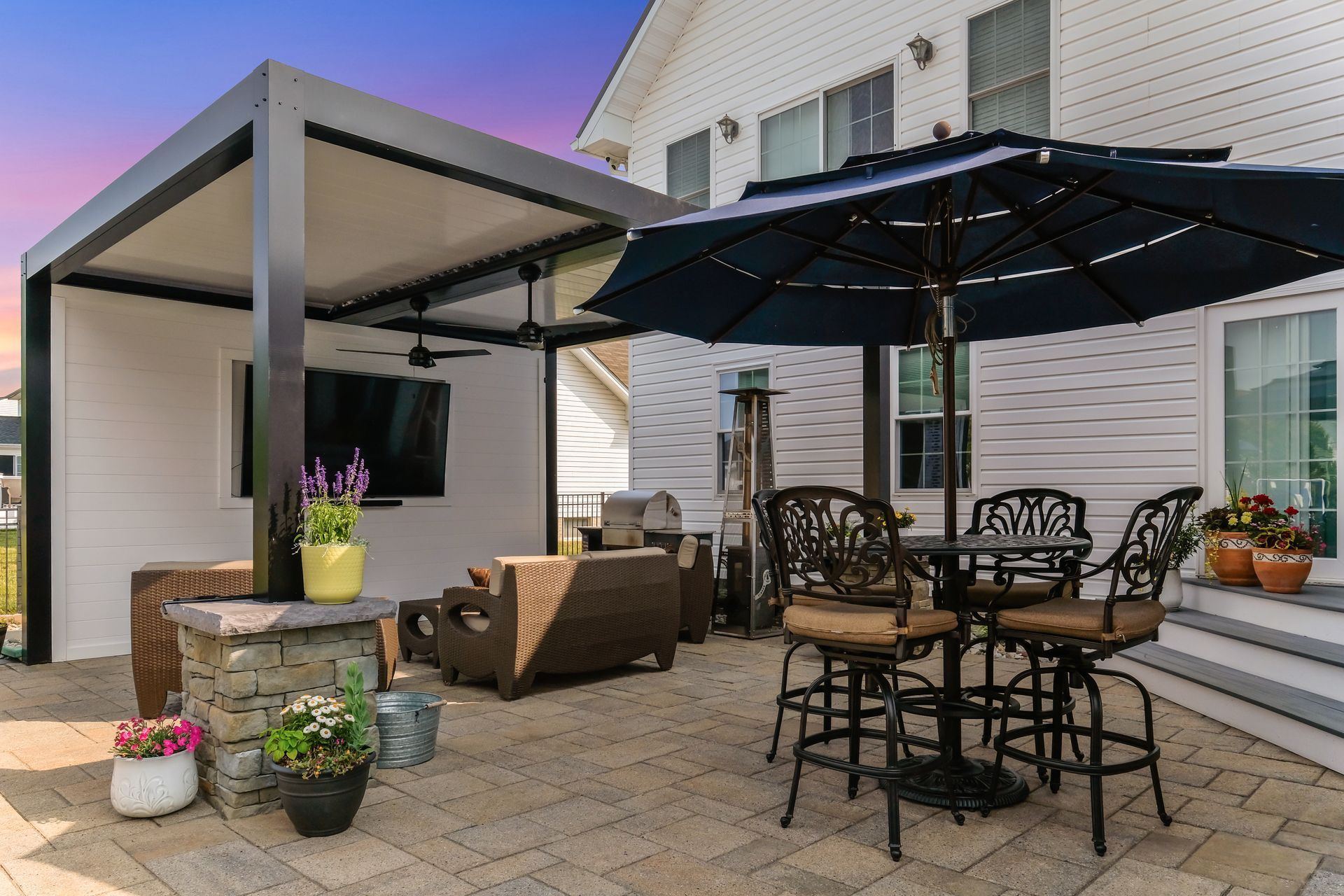 Backyard patio with outdoor dining set, lounge seating, and a covered grill area beside a house