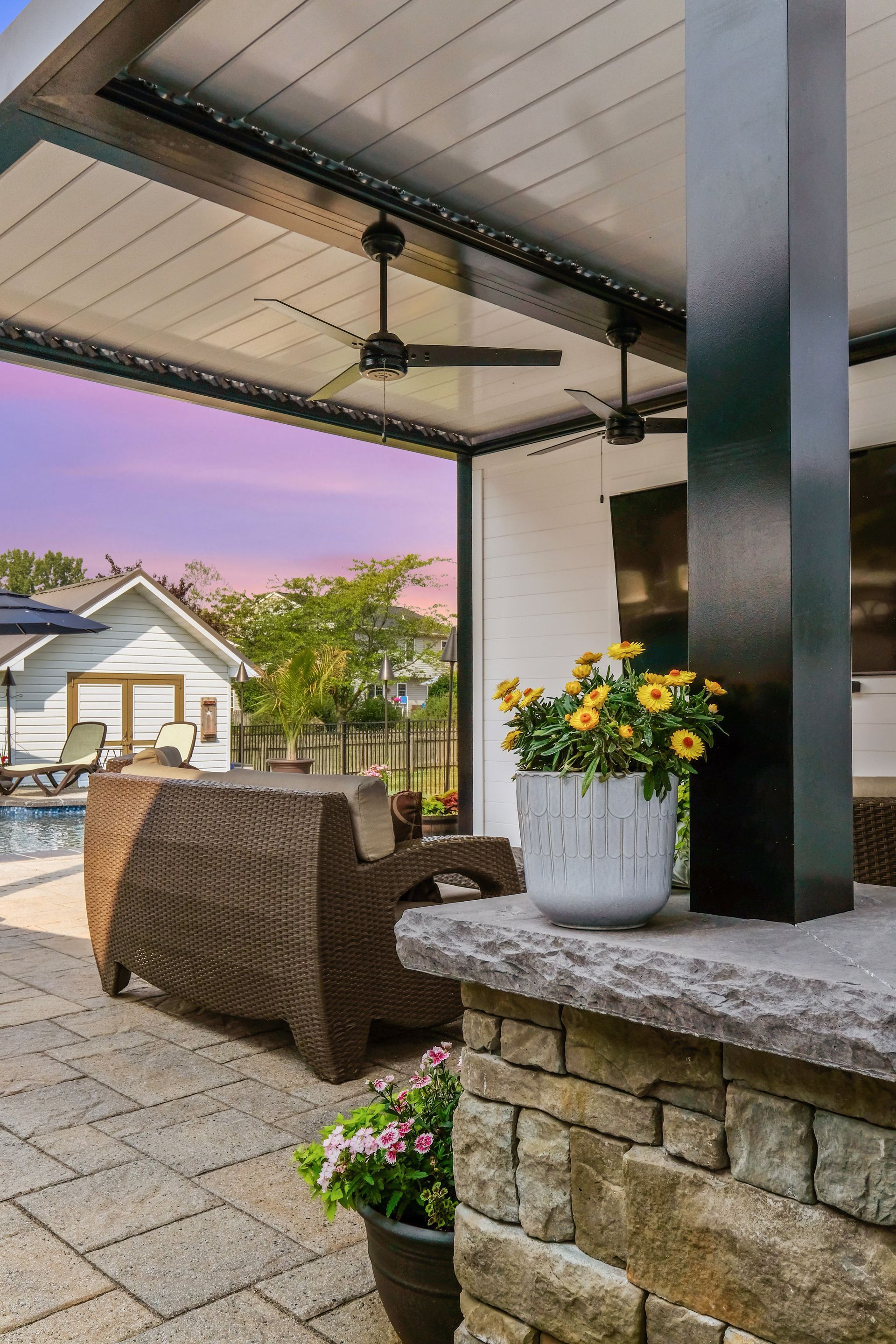 Covered patio with wicker chair, stone columns, and flower pots at sunset