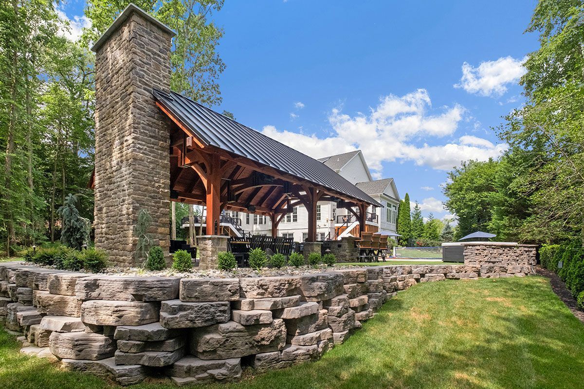 Stone pavilion with a tall chimney and wooden roof in a grassy park under a blue sky