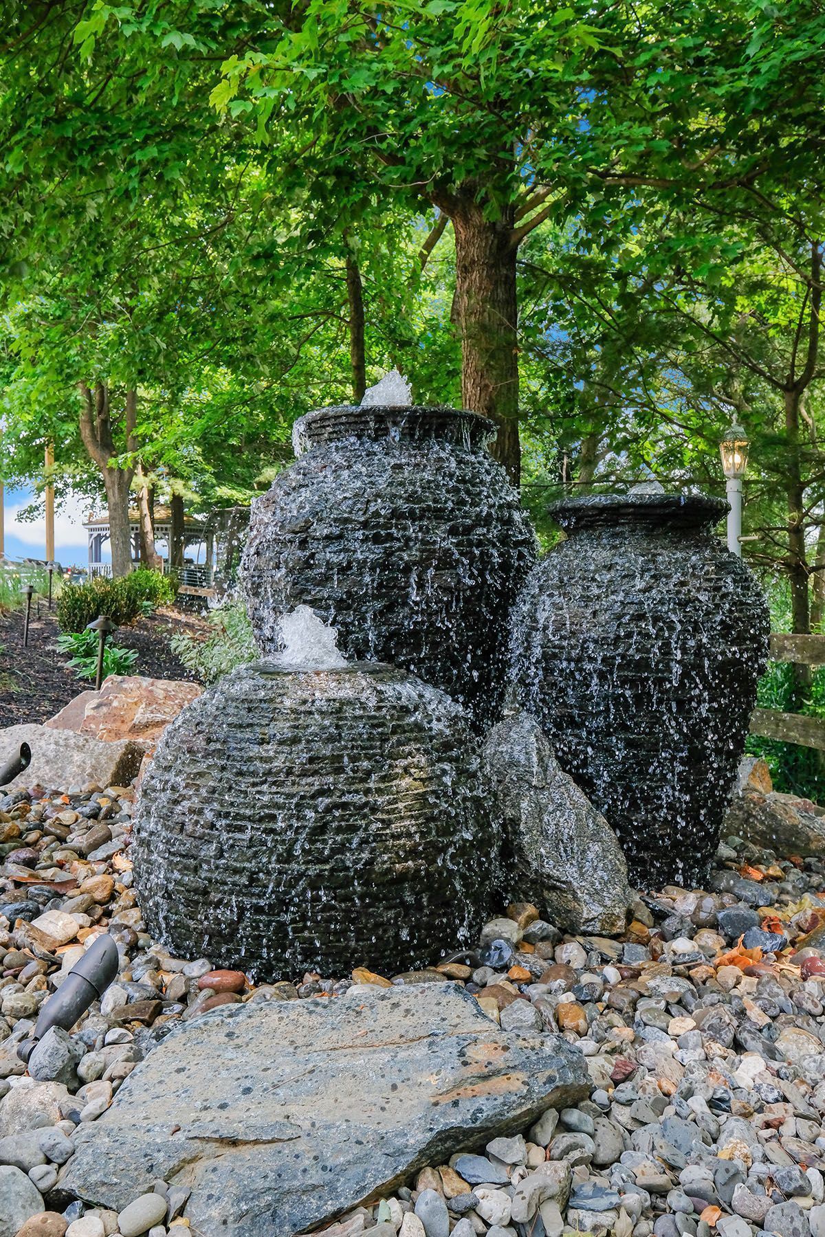Three black woven pots beside a tree in a rocky garden setting