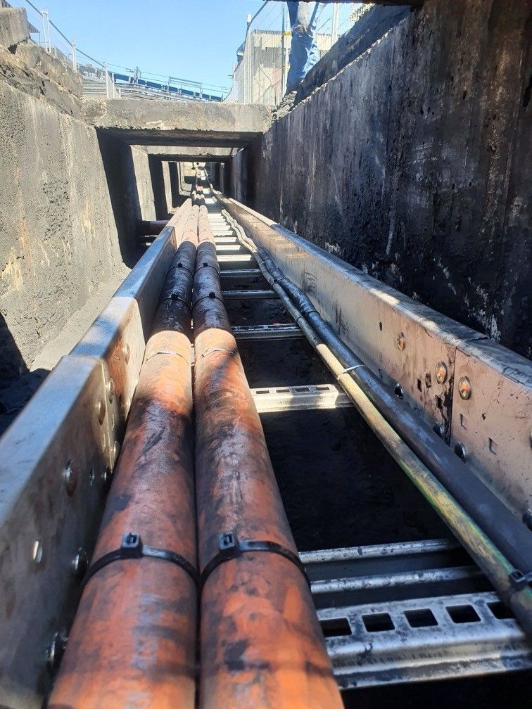 Rusty orange pipes on conveyor in a concrete industrial trench under daylight