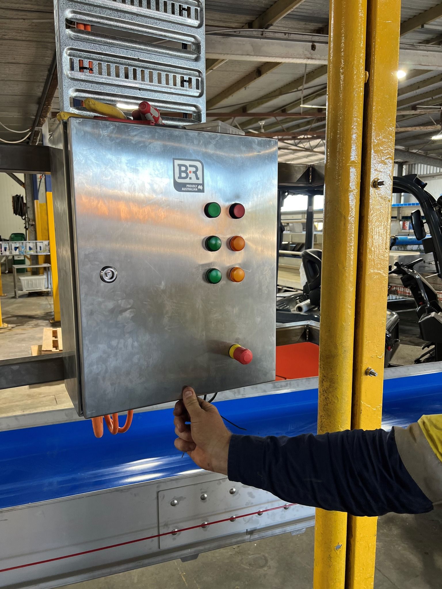Hand touching a stainless steel control panel with colored buttons in an industrial setting