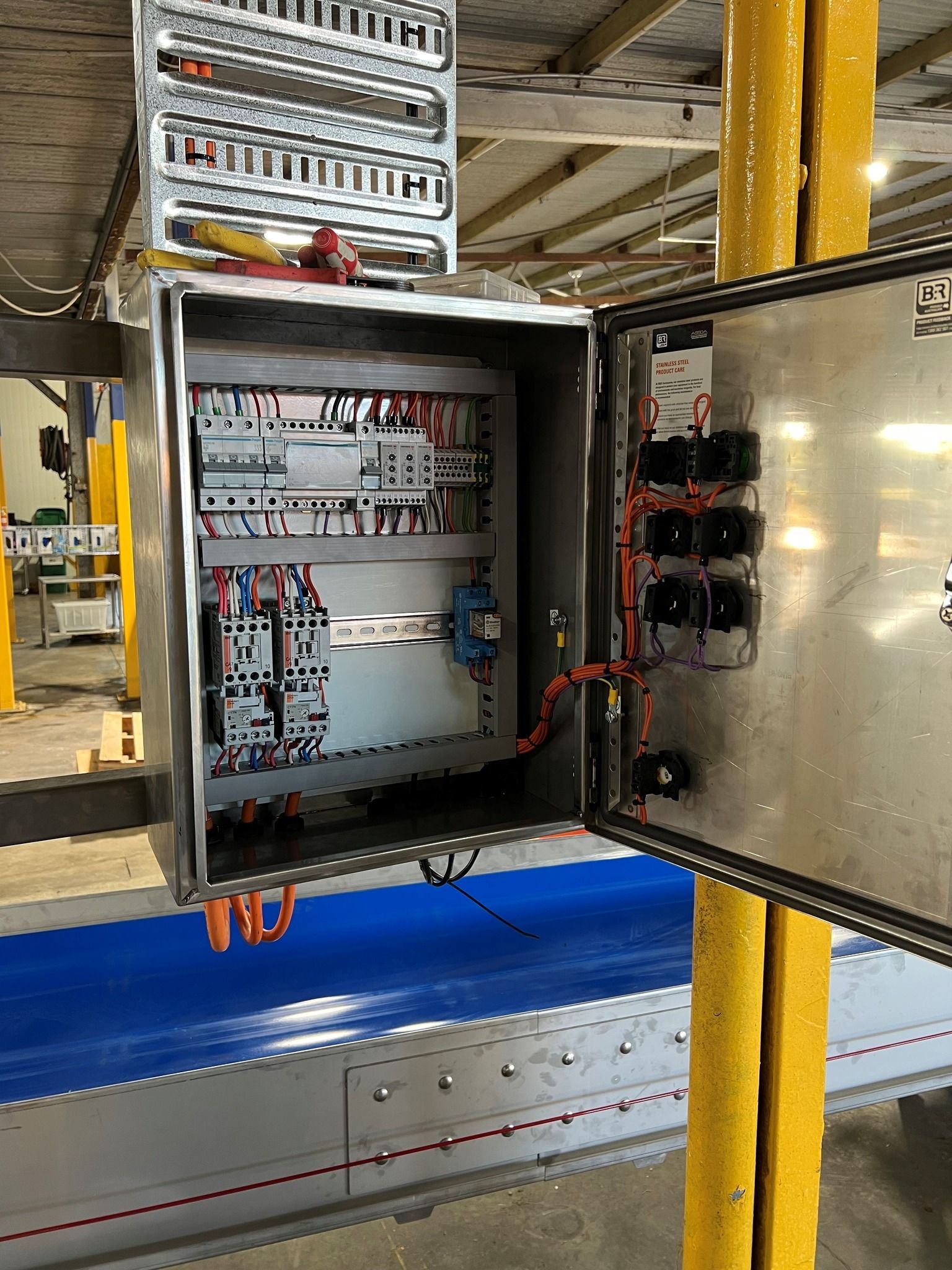 Open electrical control cabinet with wiring and circuit breakers in an industrial setting