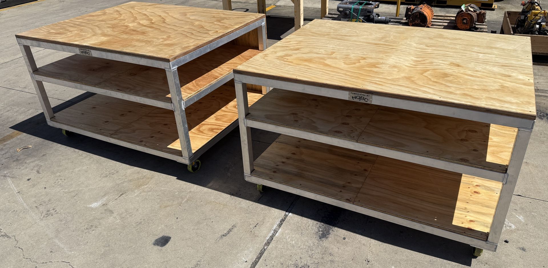 Two wooden workbenches with plywood tops on a concrete surface outdoors