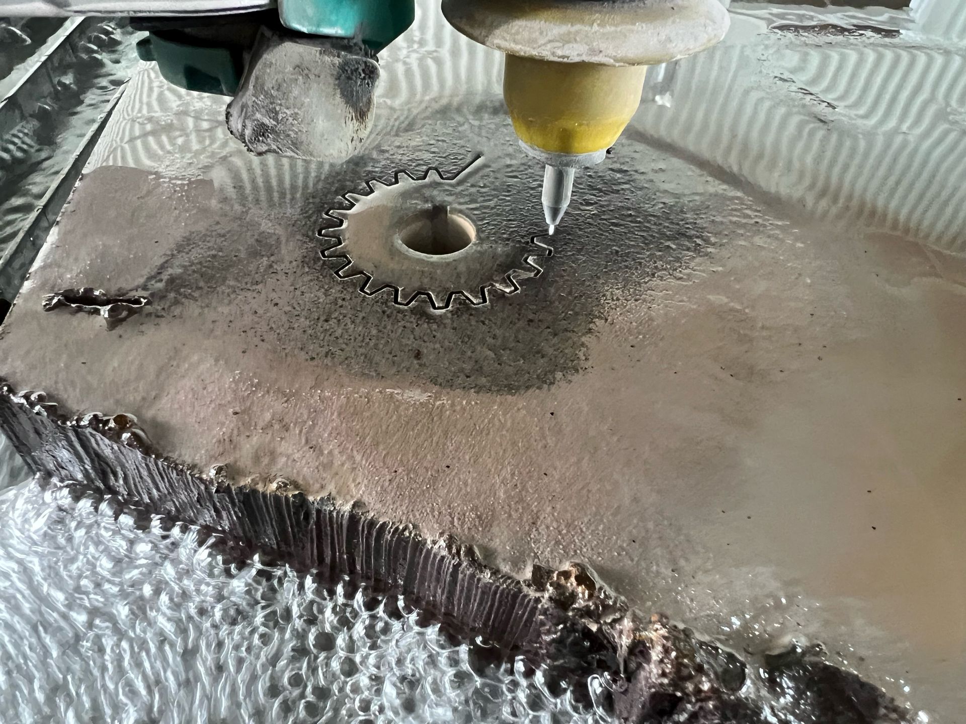 Waterjet cutting metal sheet, with a nozzle spraying water around a small circular cutout.