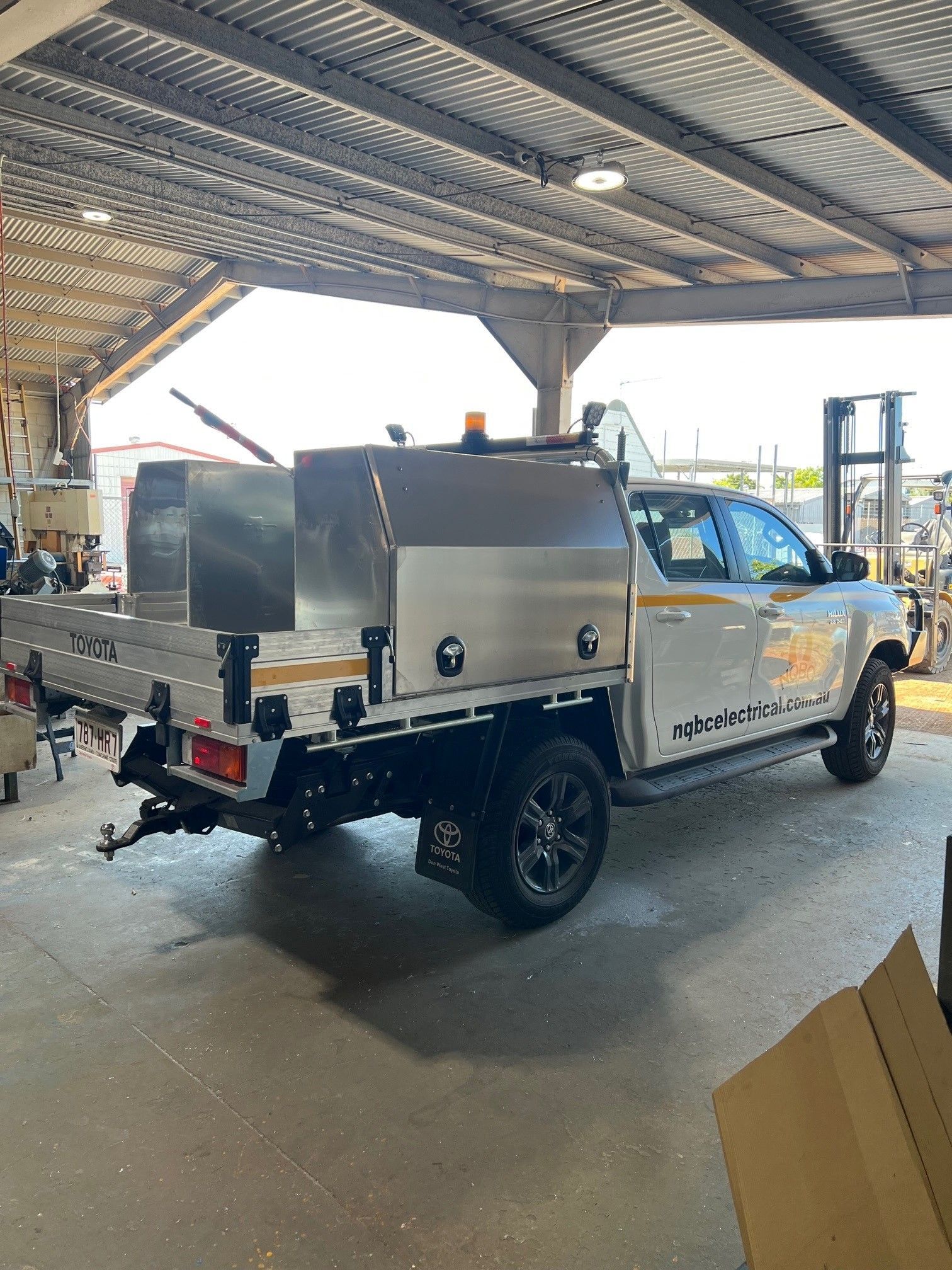 White utility truck with stainless steel service body parked under a covered work area