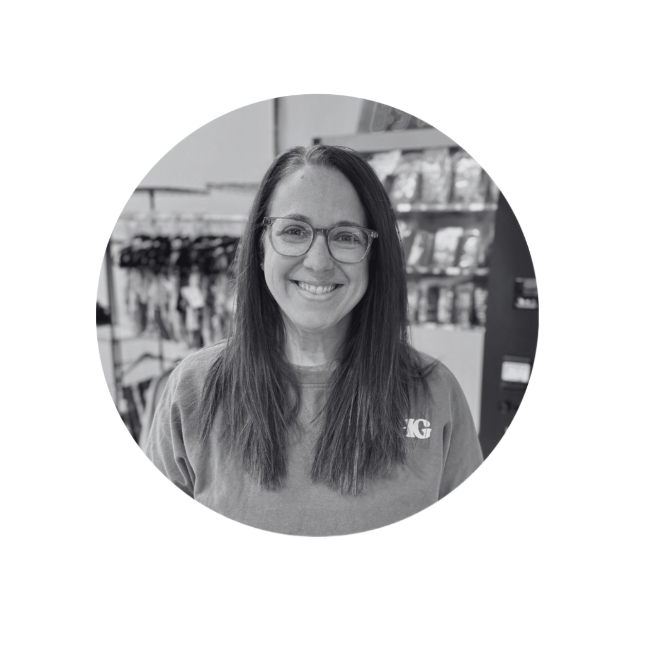 Smiling person with glasses in a store aisle, wearing a T-shirt and long hair.