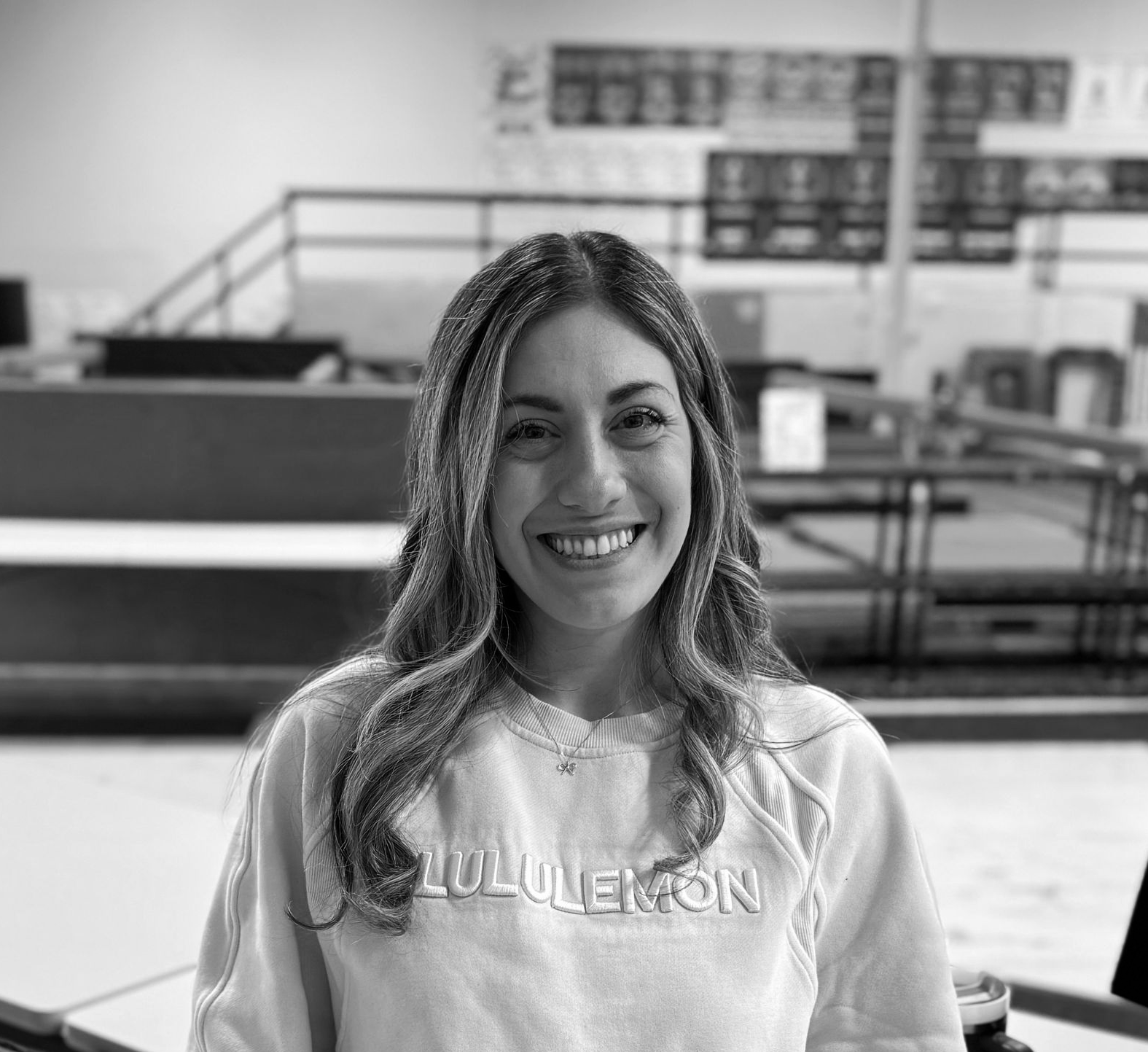Smiling person in a gym wearing a Fullerton sweatshirt, with exercise equipment in the background