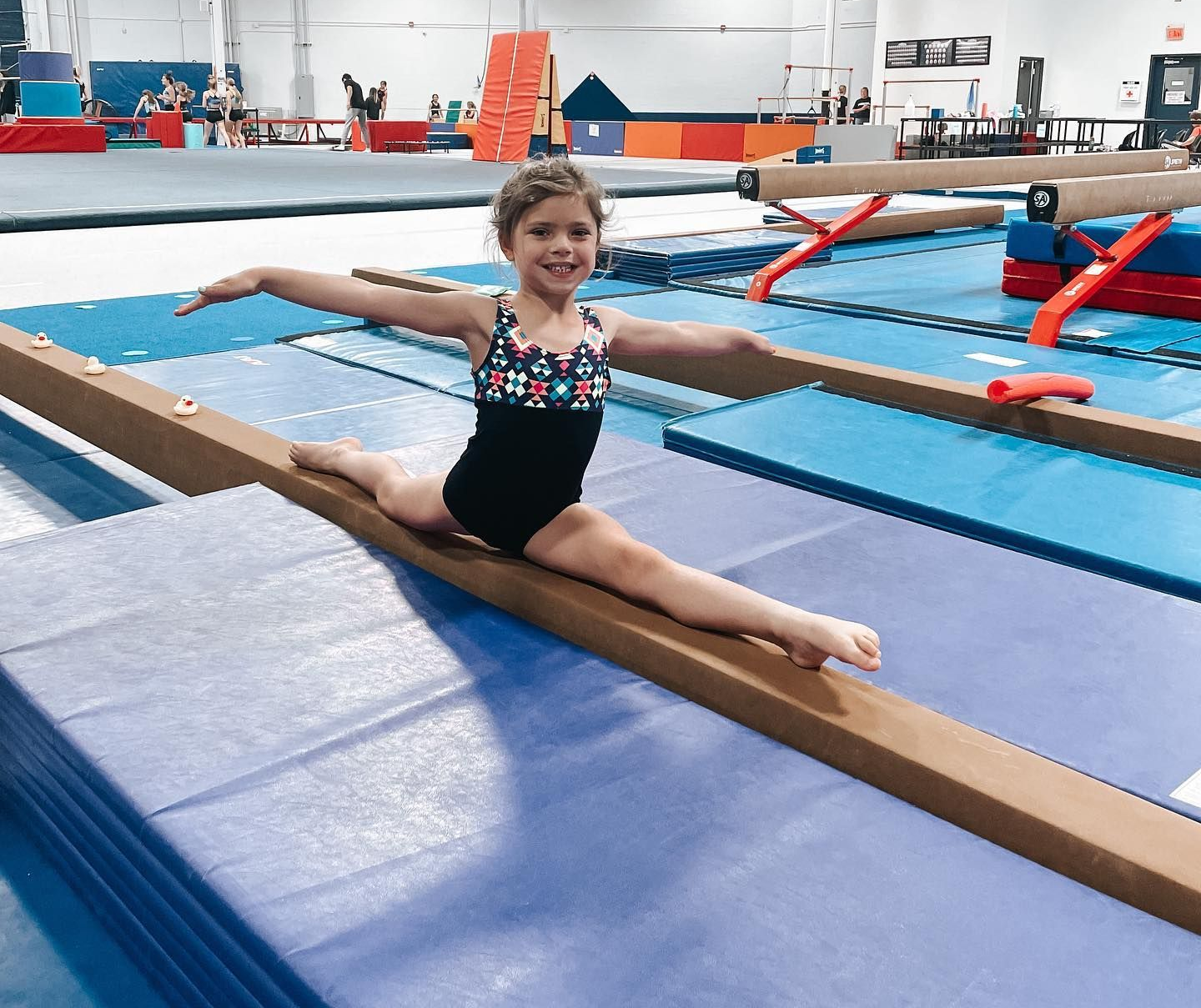 Young gymnast smiling in a split on a balance beam in a gymnasium