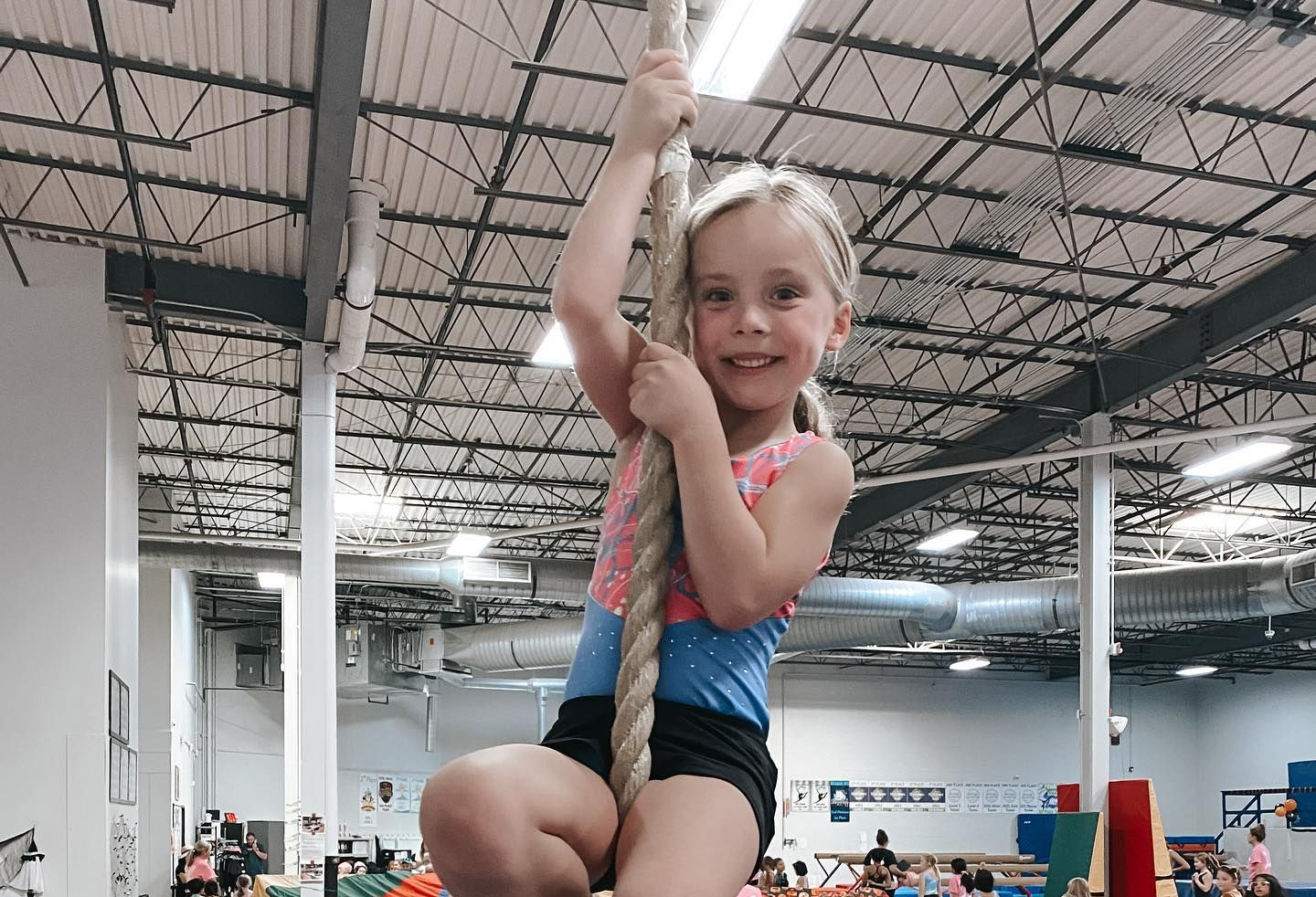 Child smiling while hanging from a rope in an indoor gym