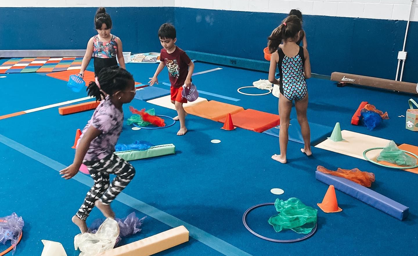 Children playing on colorful foam obstacle course in a blue-floored indoor gym