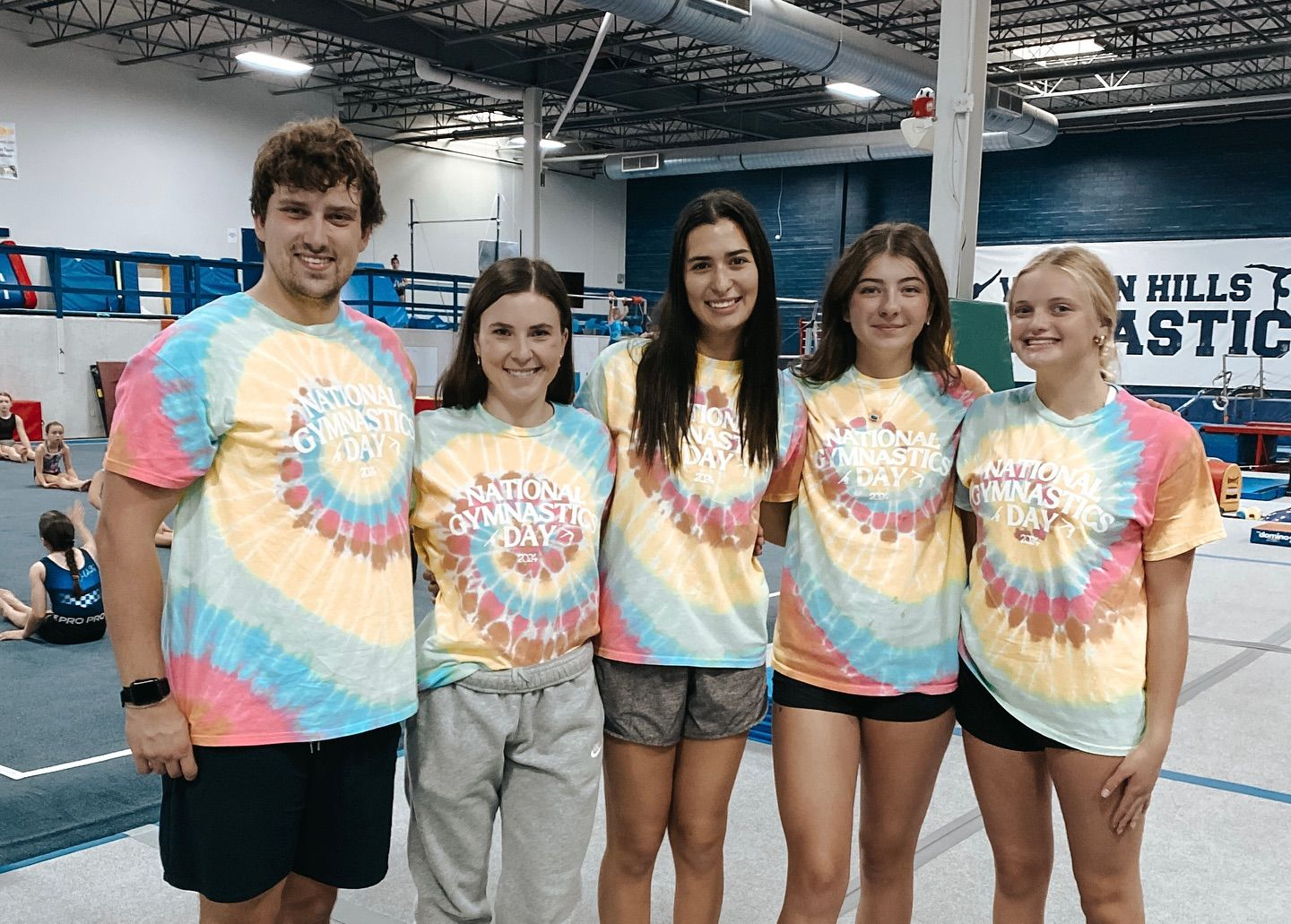 Five people in tie-dye shirts posing together indoors at a fitness event