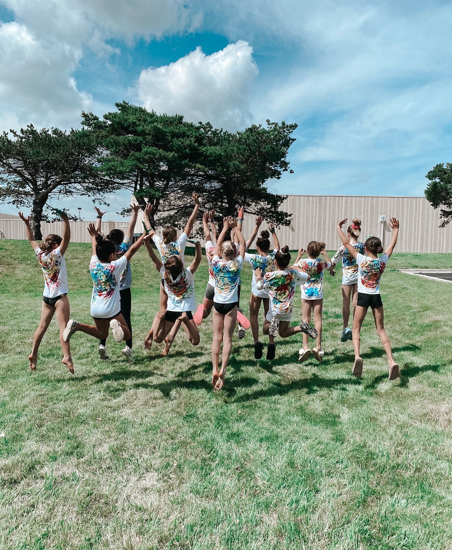 Group of children jumping with arms raised on a grassy field under a blue sky