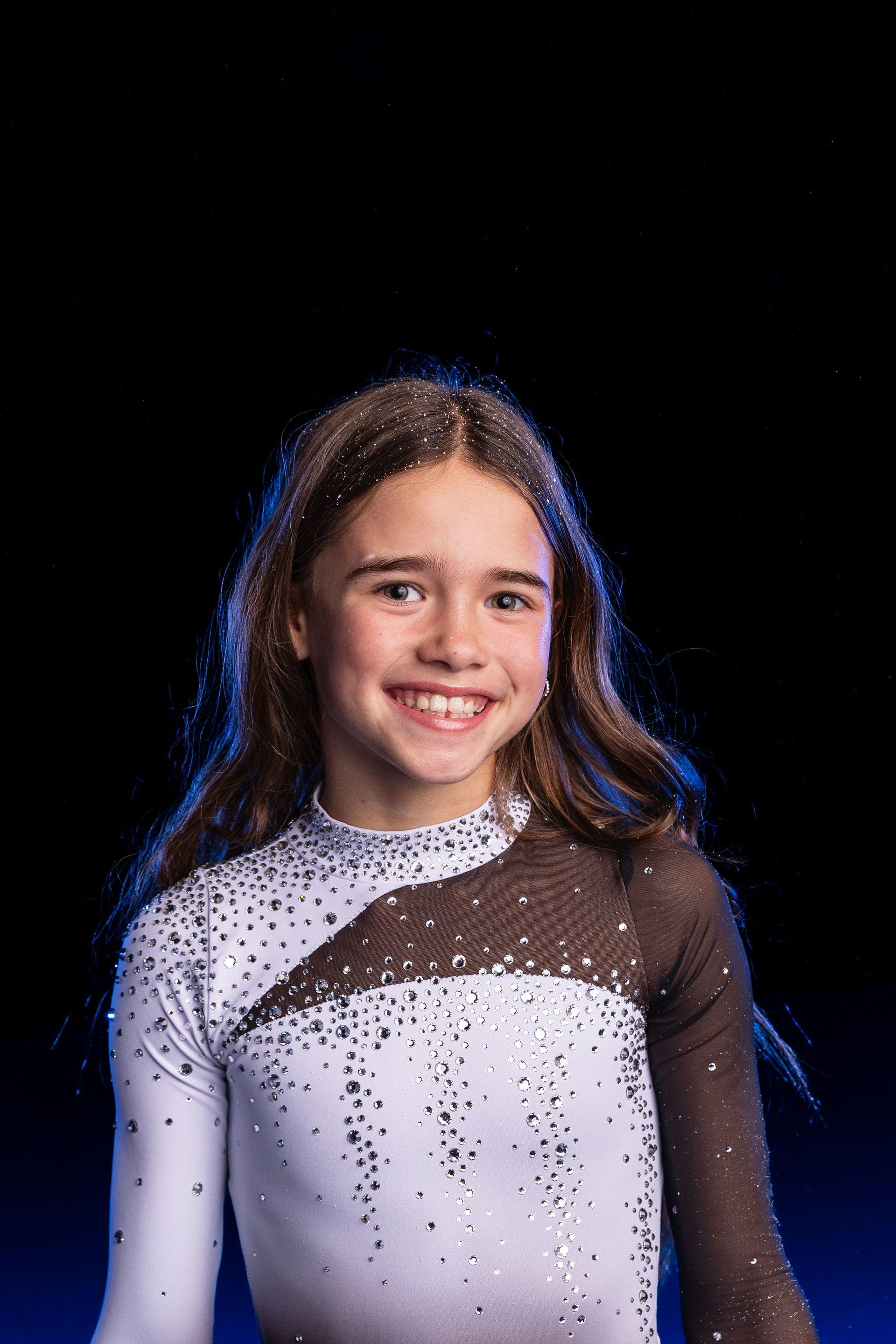Smiling person in a glittery white and brown outfit against a black background with blue edge lighting