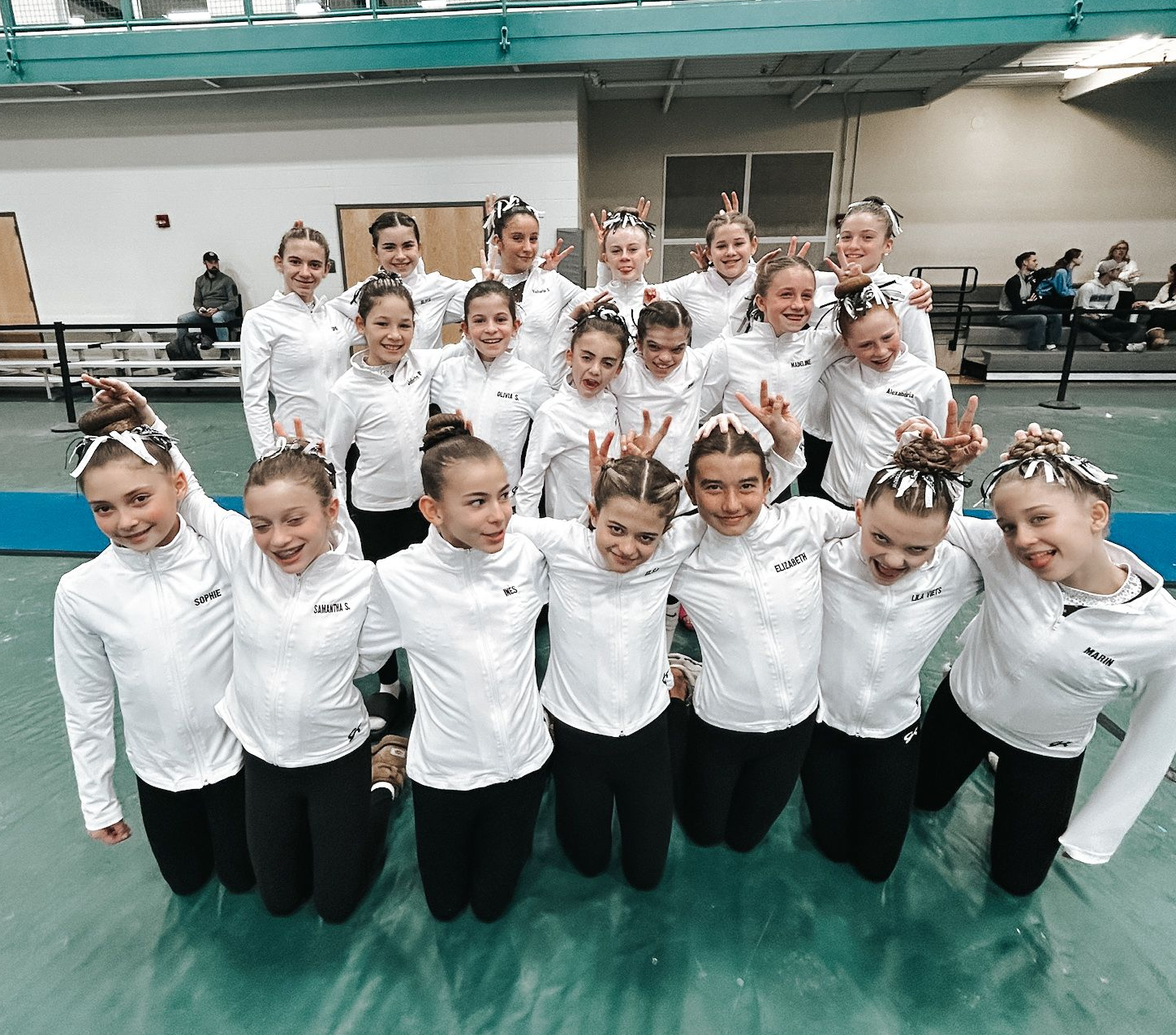 Group of synchronized dancers in white tops and black pants posing in a gymnasium