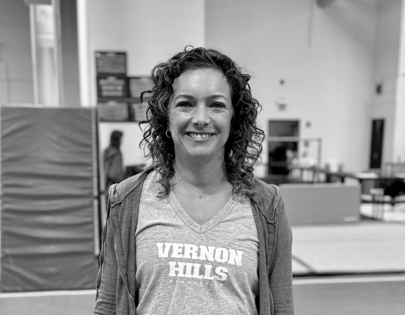 Smiling person indoors wearing a Vernon Hills T-shirt and striped cardigan
