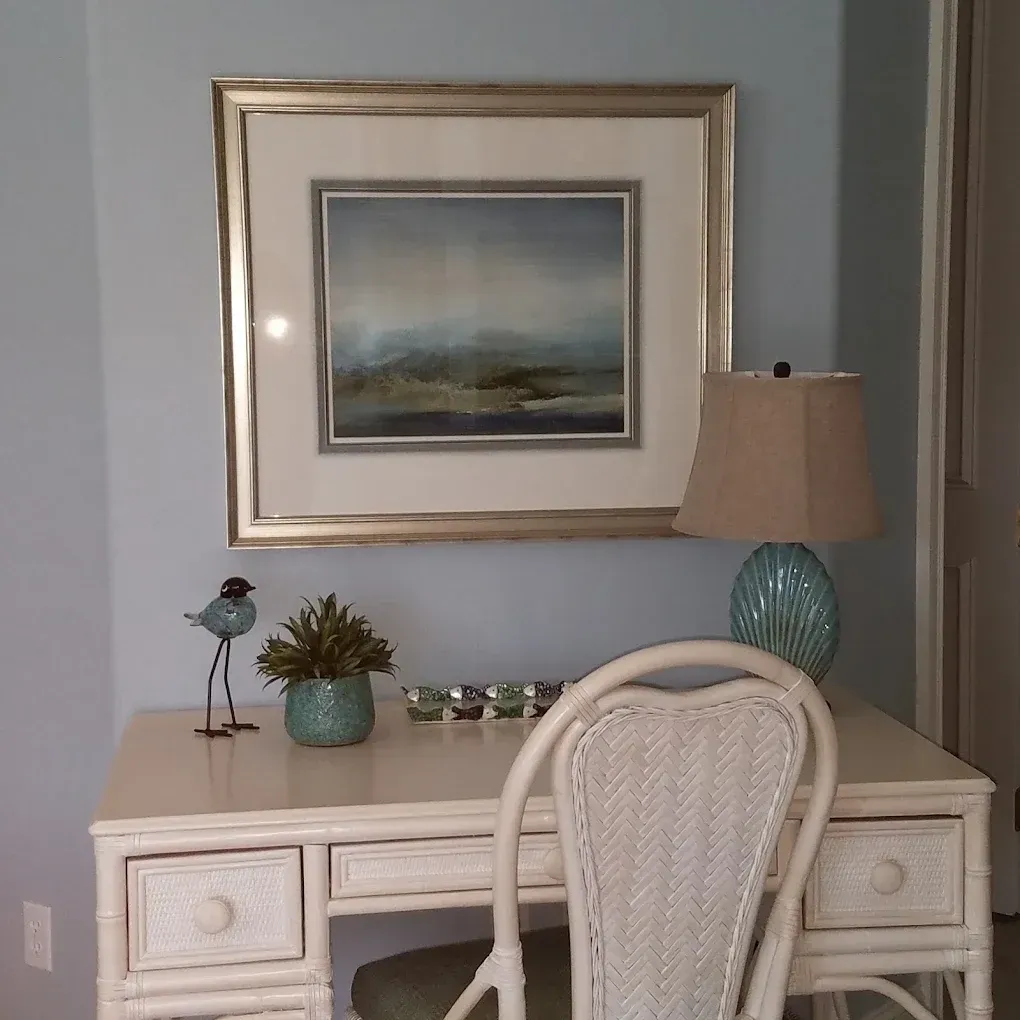 Desk with art, lamp, and wicker chair against blue wall.