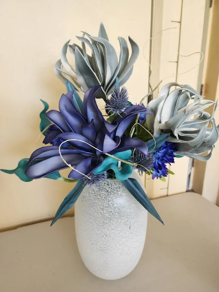 Blue and teal artificial flower arrangement in a speckled white vase.