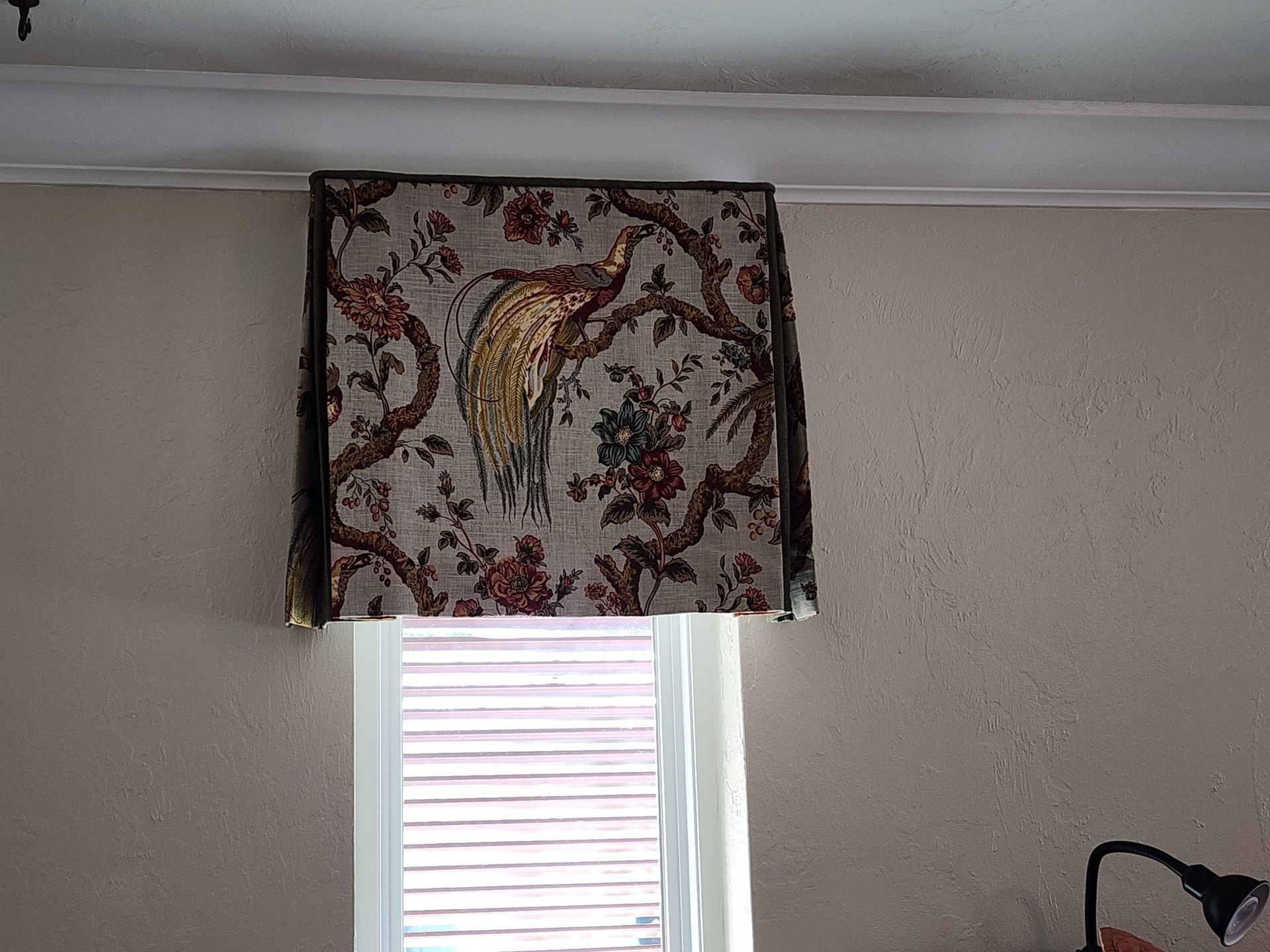 Window with fabric valance featuring a peacock design. Light beige walls.