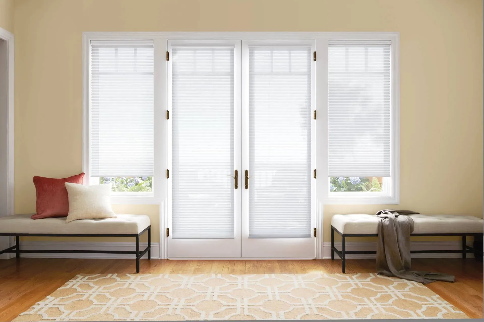 A bright room with closed white blinds, French doors, benches, and a patterned rug.