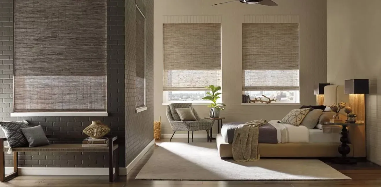 Bedroom with woven shades, neutral palette. Bed, chair, bench, and rug. Natural light.