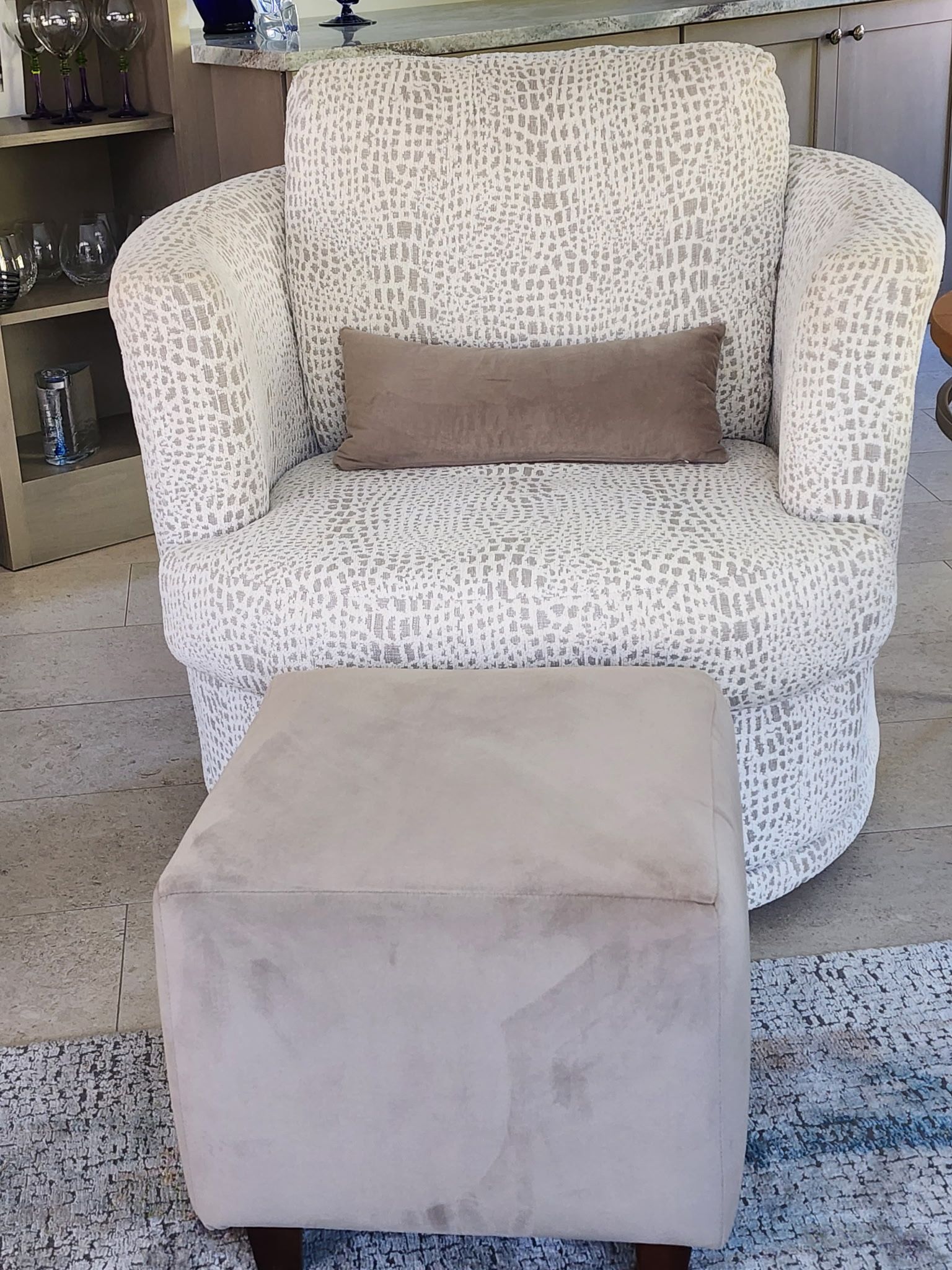 Swivel chair with patterned upholstery and a matching ottoman. A brown lumbar pillow rests on the seat.