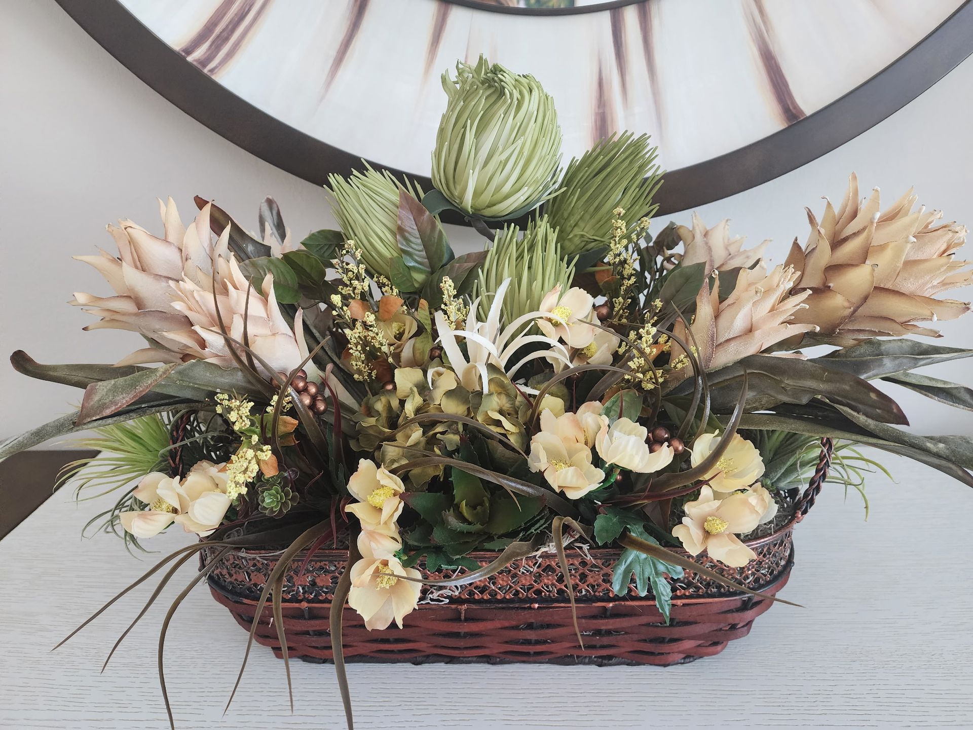 Floral arrangement in a brown basket with beige and green flowers and foliage.