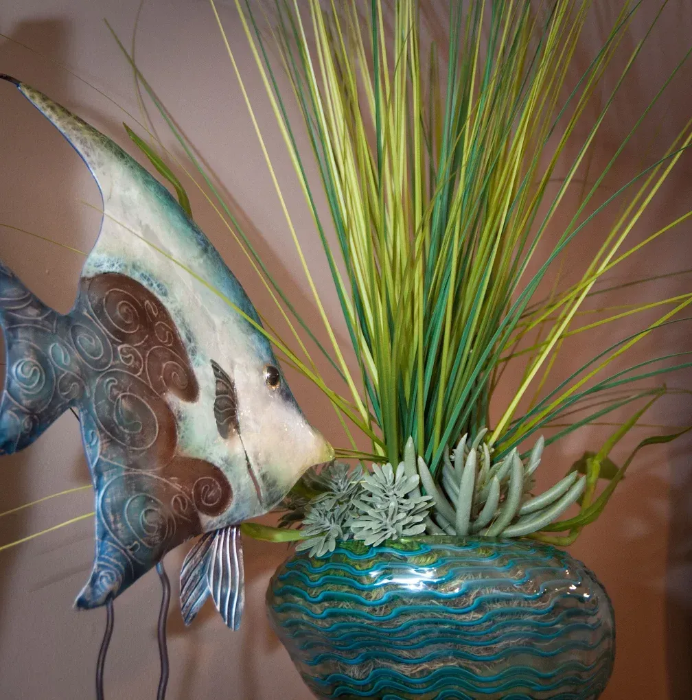 Metal fish decoration next to a teal vase with plants, indoors.