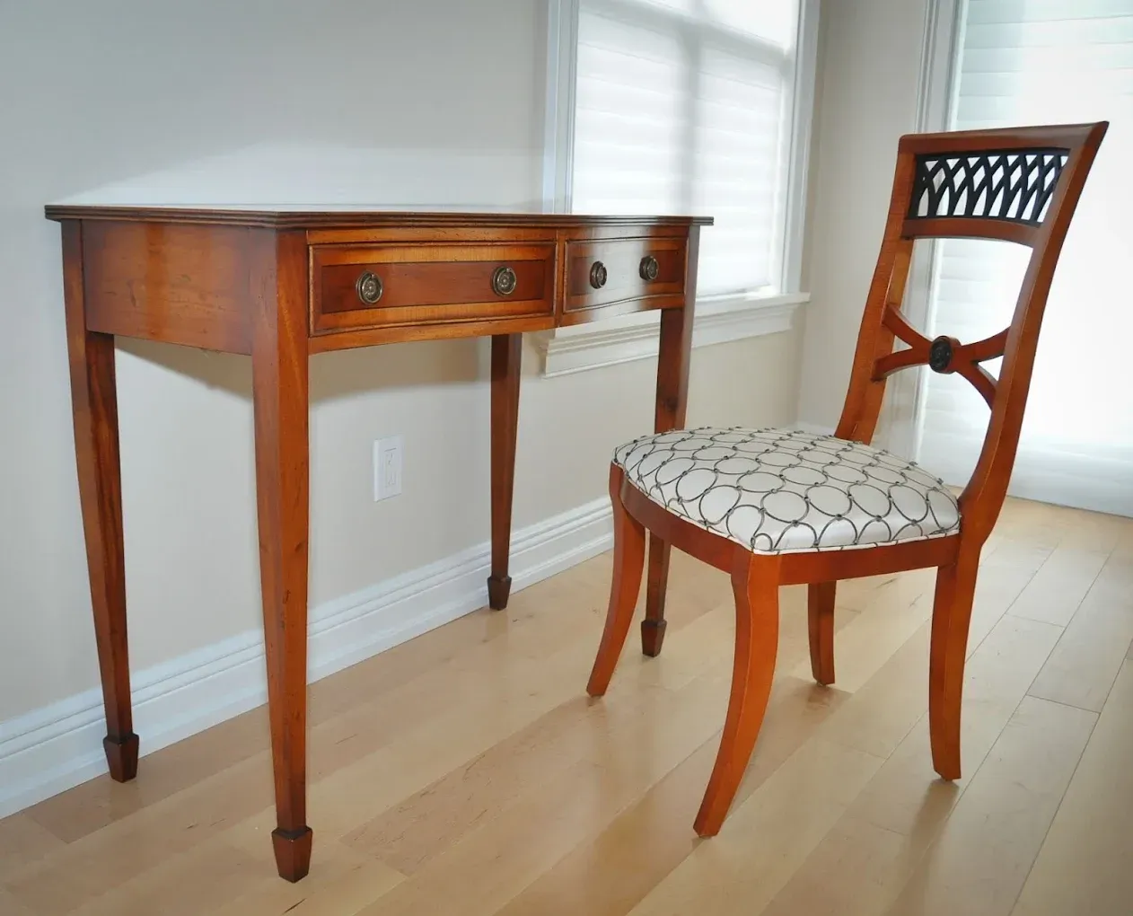 Wooden desk and chair in front of a window. The desk has a drawer. Chair has a patterned seat and decorative back.