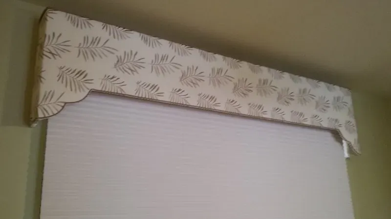 Window with a cream-colored cellular shade and a decorative valance with a leaf pattern.