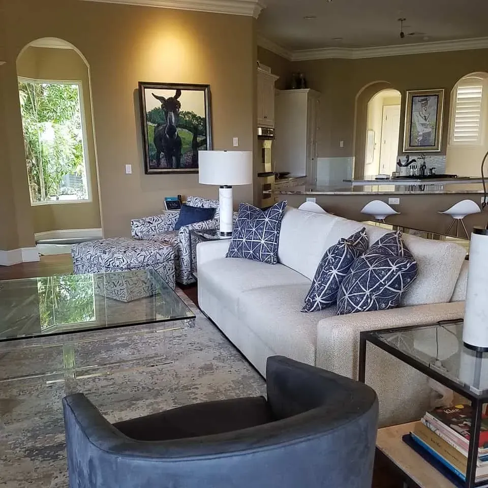 Living room with a sofa, patterned ottoman, glass coffee table, and artwork.