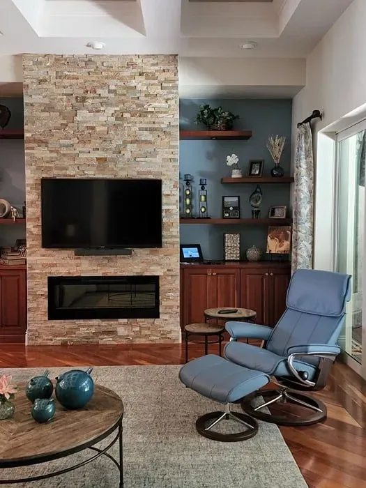 Living room with stone accent wall, fireplace, TV, built-in shelving, blue recliner, and wooden coffee table.
