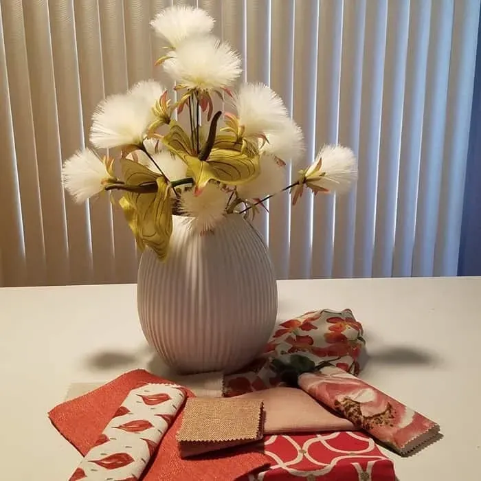 White vase with floral arrangement on white table, surrounded by colorful fabric swatches.