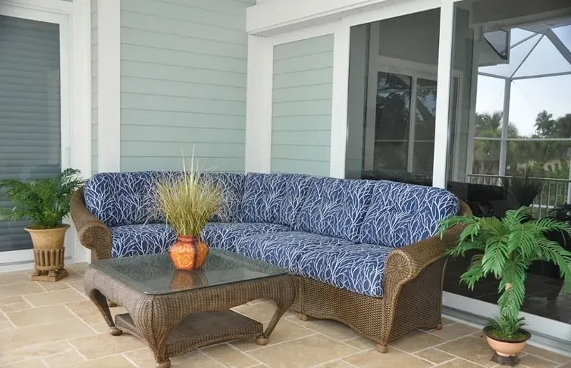 Outdoor living space with blue patterned sectional sofa, wicker furniture, and potted plants.