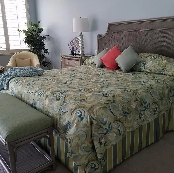 Bedroom with bed, bench, armchair, and nightstand. Floral bedspread, green striped bed skirt, and blue walls.