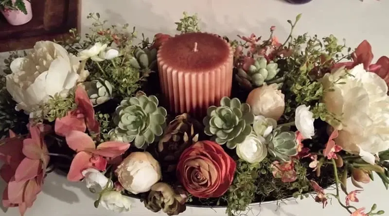 Centerpiece with a copper candle surrounded by flowers and succulents.