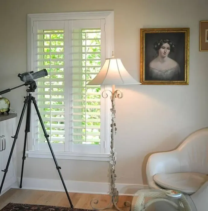Interior with a telescope on tripod, window with shutters, portrait, lamp, and chair.