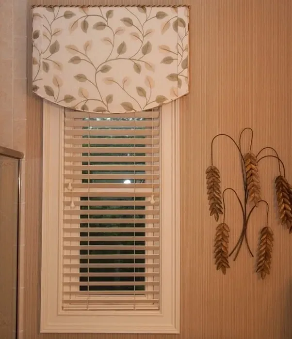 Window with blinds and a fabric valance, beige and green floral pattern. Wall decor of metallic gold wheat.