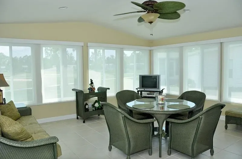 Sunroom with cream-colored walls, green furniture, large windows, and a ceiling fan.