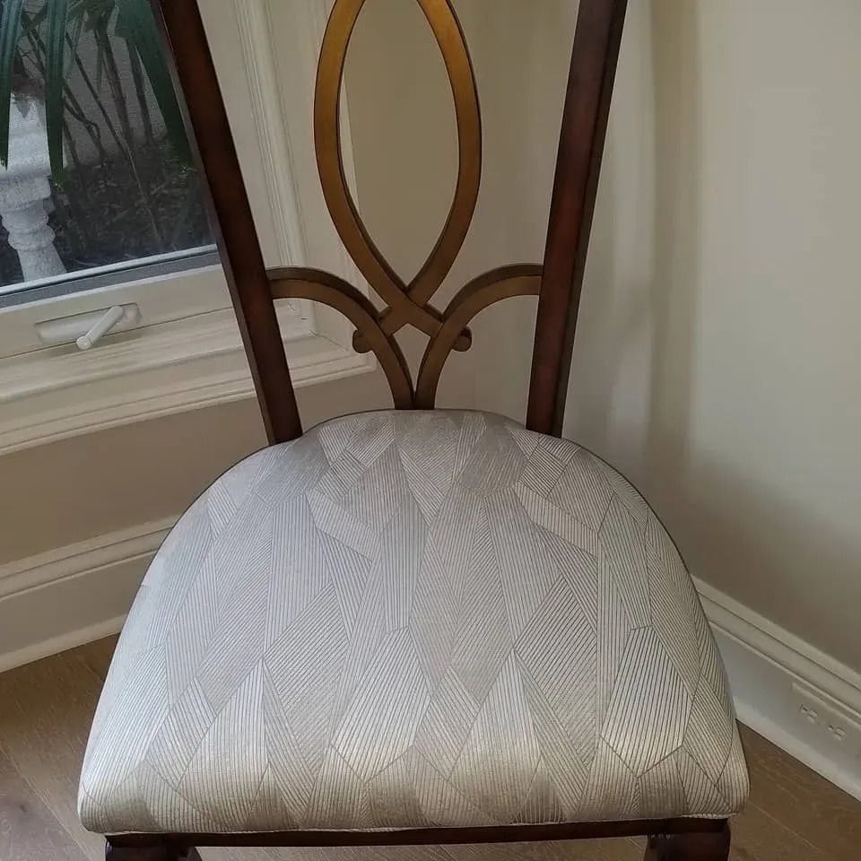Wooden dining chair with a gold design on the back and a patterned, upholstered seat.