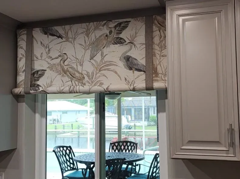 Roman shade with heron and foliage pattern above a glass door.