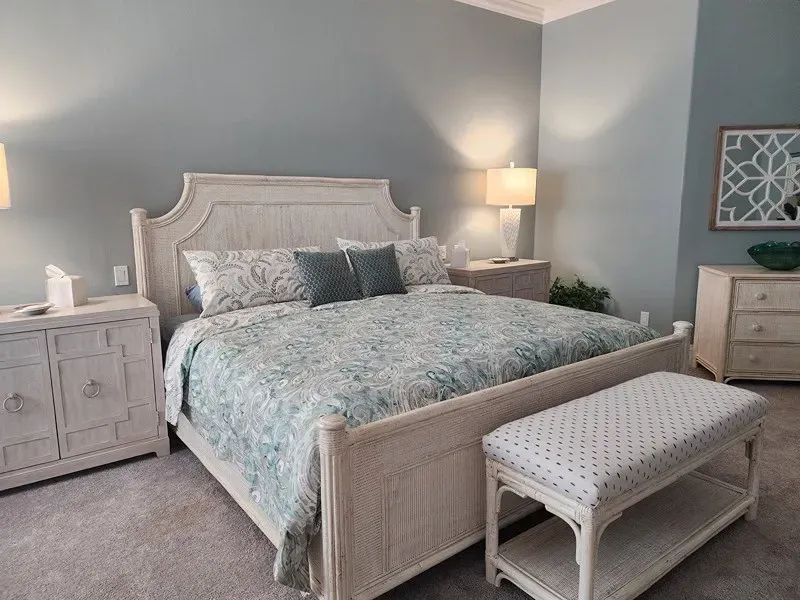 Bedroom with white wicker furniture, blue-green bedding, and light blue walls.