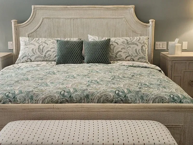 Bedroom with a white bed frame, floral bedding, two teal pillows, and a bench.
