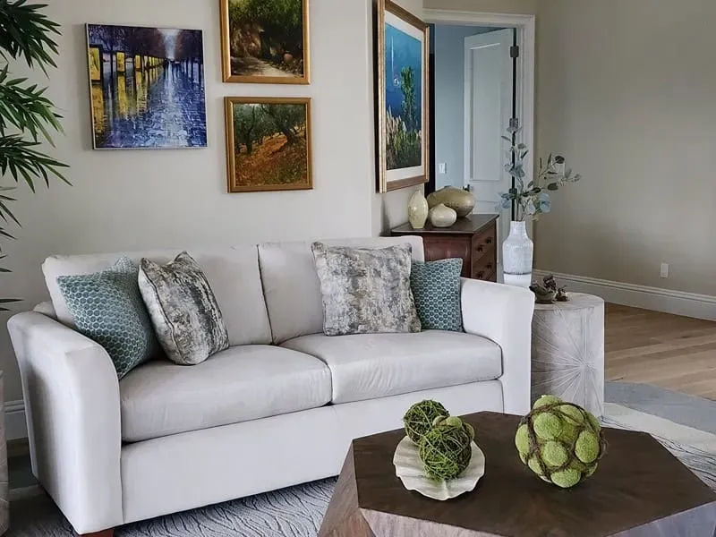 Living room with white sofa, art on the wall, side table, coffee table, and plants.